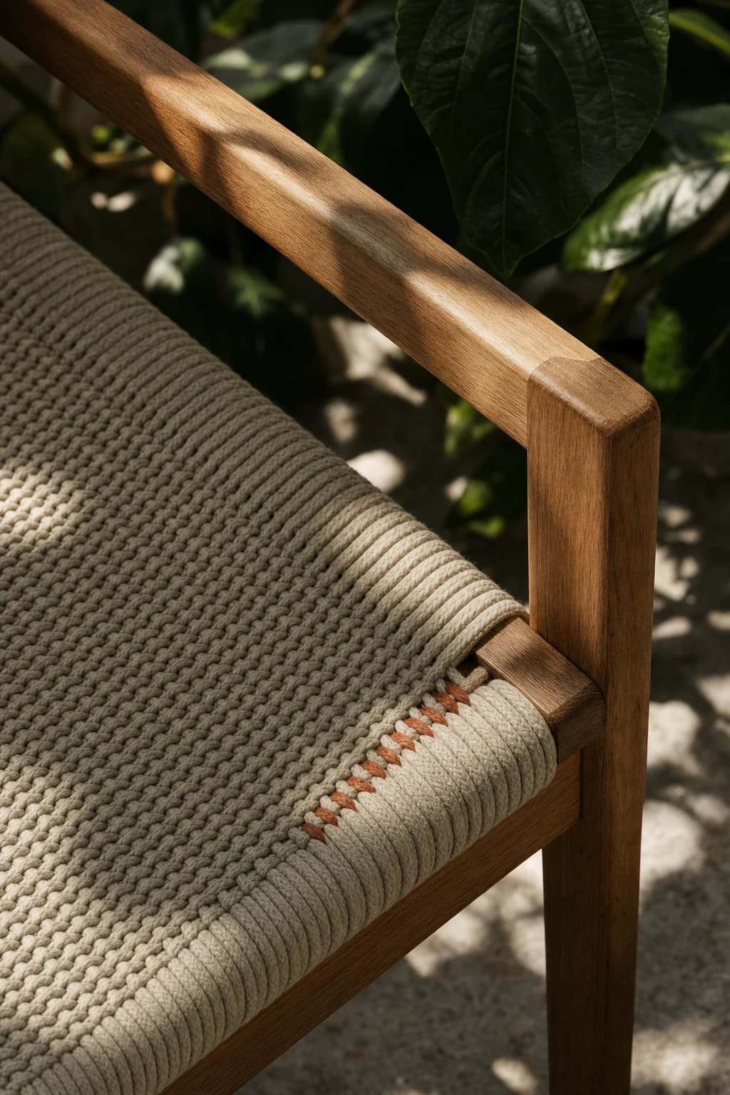 Close detail of a woven chair seat and warm timber armrest with leaf shadows